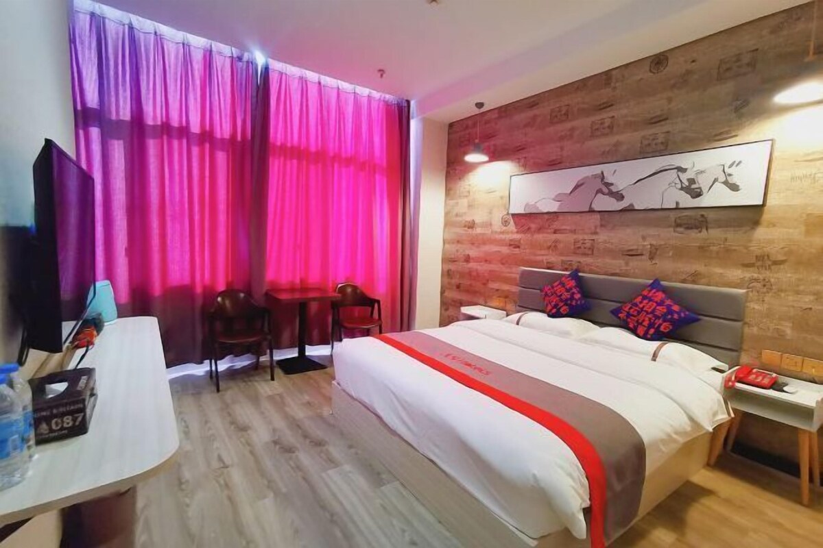 Habitación de hotel con cama, escritorio, silla, televisión y ventana con cortinas.