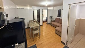 A compact living space with a kitchenette, a dining area, a sofa, and a door leading to a bathroom.