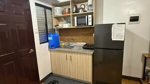 A compact kitchen with a black refrigerator, wooden cabinets, a microwave, and a coffee maker.