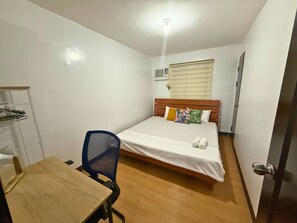 Una habitación pequeña y limpia con una cama individual, un escritorio y una silla.