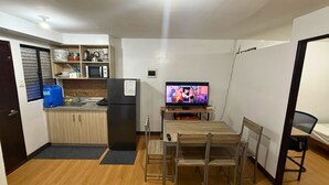 A compact kitchen with a refrigerator, microwave, and sink. A dining table with chairs is positioned in front of a television.