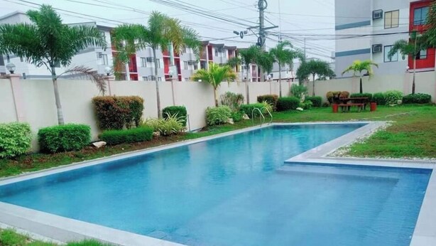 A rectangular swimming pool with a tiled edge, surrounded by well-maintained greenery and a low wall.