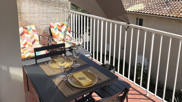Ein Balkon mit Tisch für Zwei, Gartenmöbeln und Blick auf umliegende Gebäude.