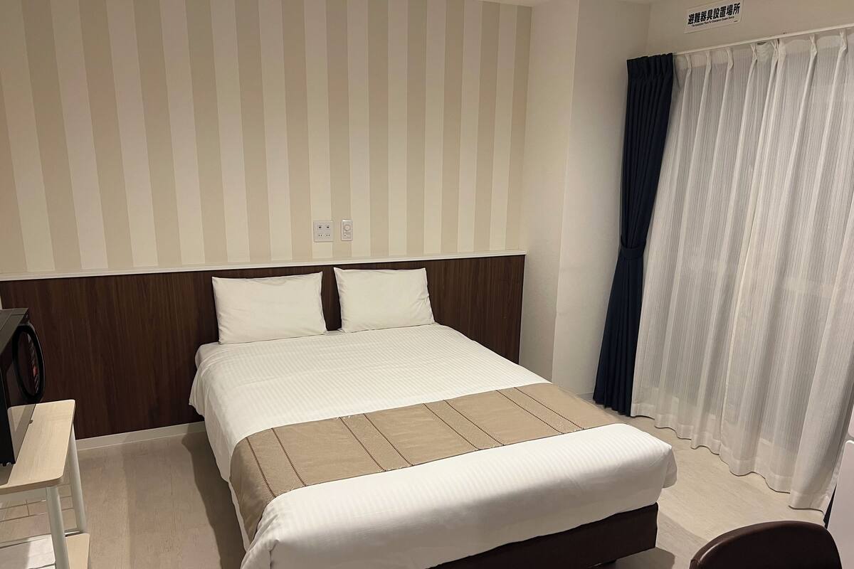 A hotel room with a large bed, a wooden headboard, a bedside table, and a chair.