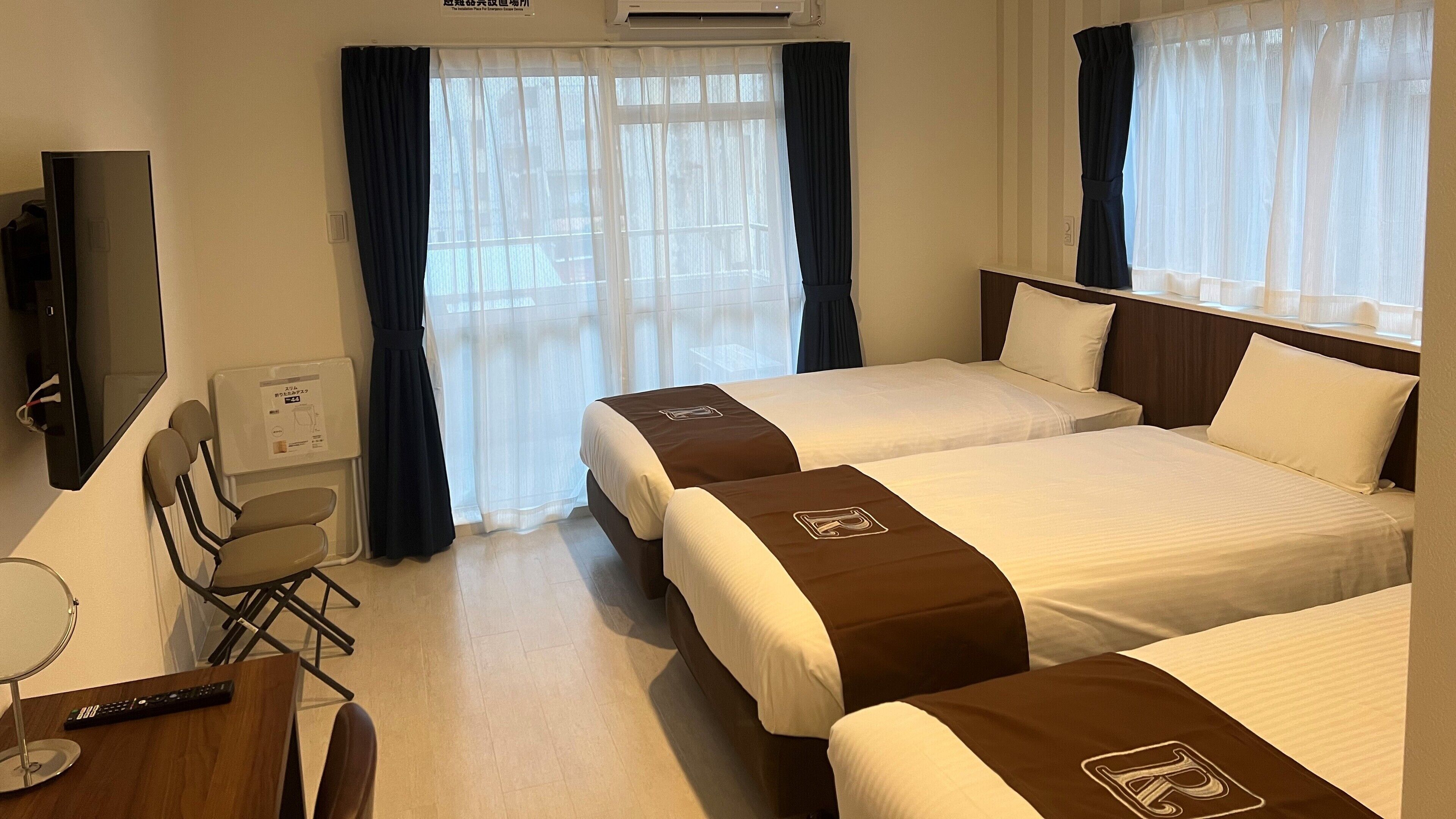 Una habitación de hotel con dos camas, un escritorio con silla, televisor y aire acondicionado.