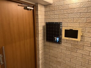 Une chambre d’hôtel avec une porte en bois, un climatiseur fixé au mur et un écran numérique affichant des informations sur la chambre.