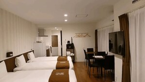 Ein Hotelzimmer mit zwei Betten, einem Schreibtisch, einem Sessel, einem Fernseher und einer Küchenzeile.