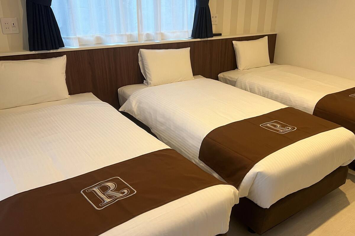 A hotel room with three single beds, each with a brown headboard and a white bedspread.