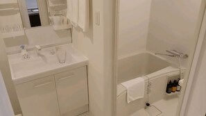 Une salle de bain avec un lavabo blanc, un miroir et un espace douche équipé d’un porte-serviettes.