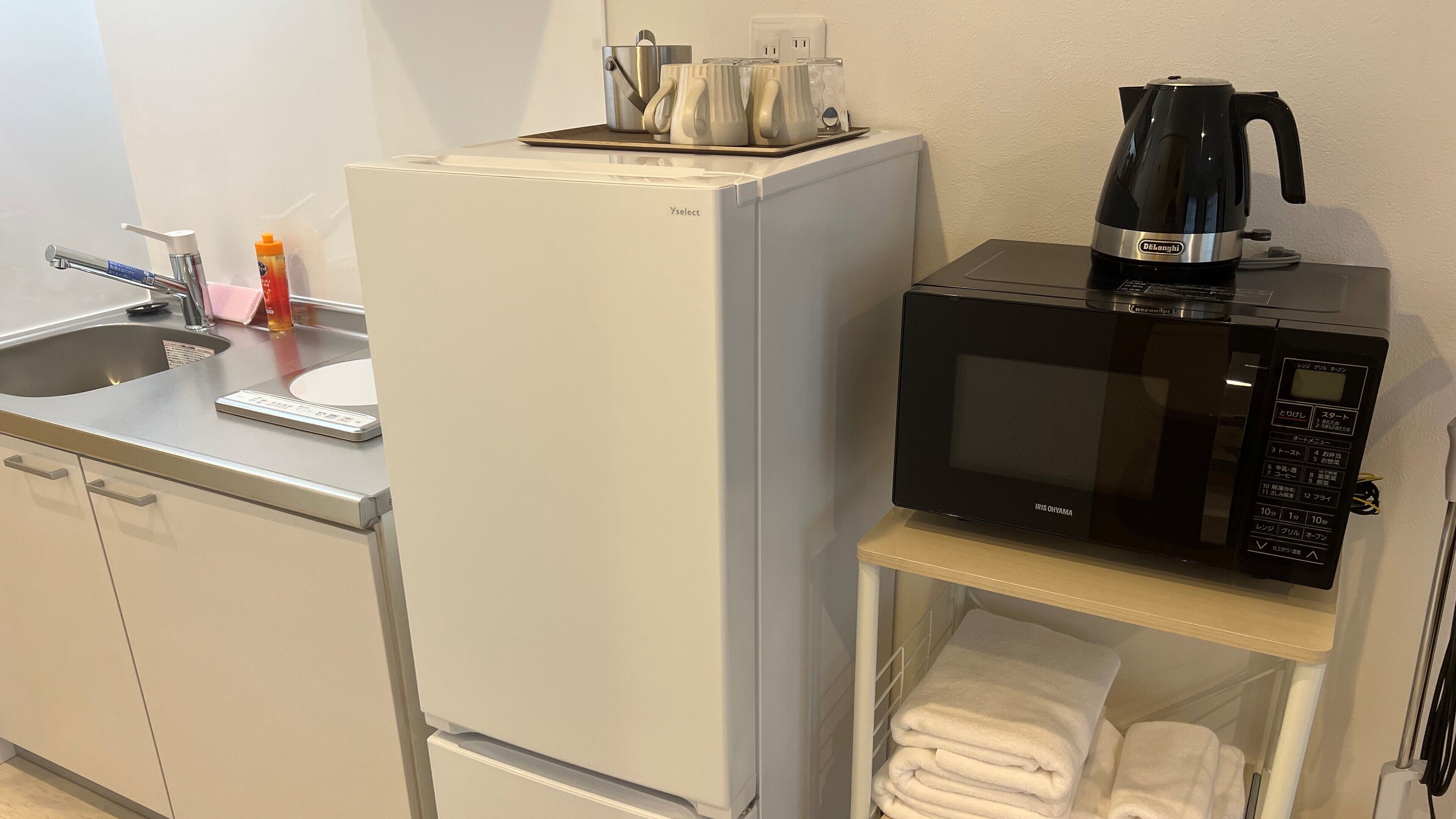 Una kitchenette compacta con un refrigerador blanco, un microondas, una cafetera y un lavabo con grifo.