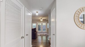 A hallway with a ceiling fan, a round mirror, and a door leading to a room with a patterned rug. - Stylish townhome, sleeps 8, pet friendly.  (Augusta)
