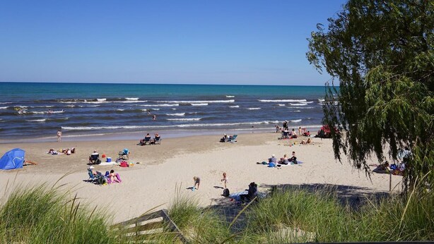 Una spiaggia con persone che si rilassano e prendono il sole, un cielo sereno e l'oceano.