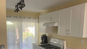 Una cucina compatta con piano cottura a gas, forno e pensili bianchi. C'è una macchina da caffè sul bancone e una tenda copre la finestra.