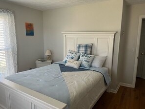 Une chambre à coucher avec un lit, une table de chevet, une lampe et un mur orné d’un tableau.