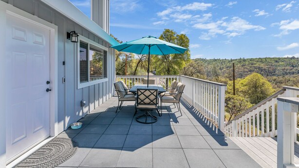 Une terrasse couverte avec une table et des chaises, un parasol bleu et une vue sur un paysage vallonné.
