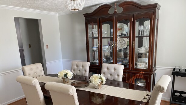 A dining room with a wooden table, six upholstered chairs, and a china cabinet.