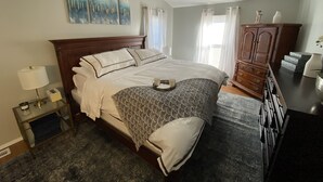 A neatly arranged bedroom with a large bed, a wooden dresser, and a nightstand with a lamp.
