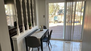 A dining area with a table and chairs, a view of the backyard through a sliding glass door, and a white railing with turned columns.