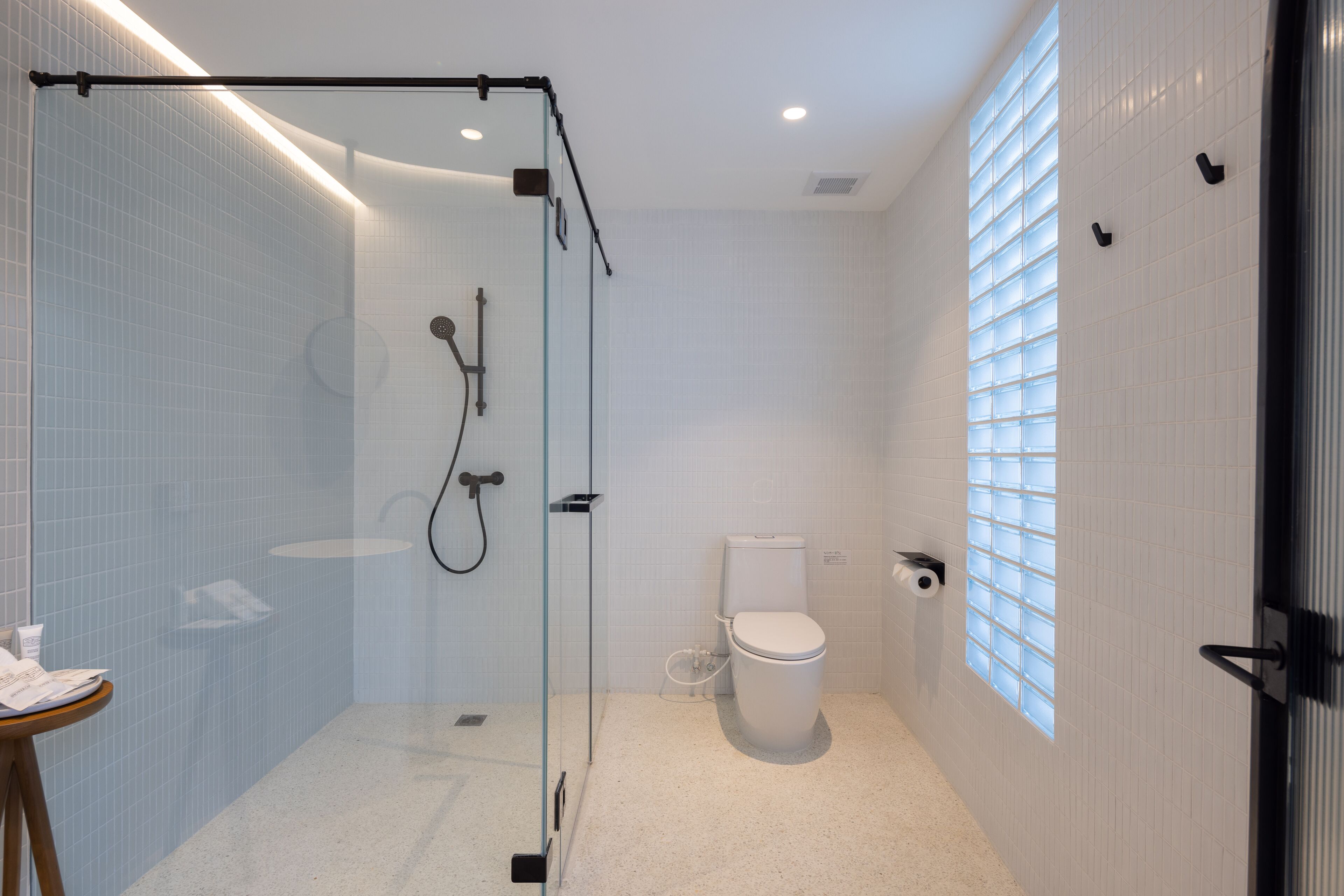 Un baño moderno con ducha acristalada, inodoro y ventana con persianas.