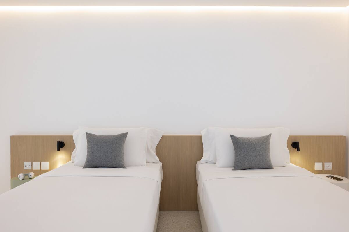 A hotel room with two single beds, each with a pillow and a bedside table.