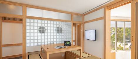 A traditional Japanese room with tatami flooring, a low wooden table with a tablet and book, and a sliding glass door leading to a balcony.