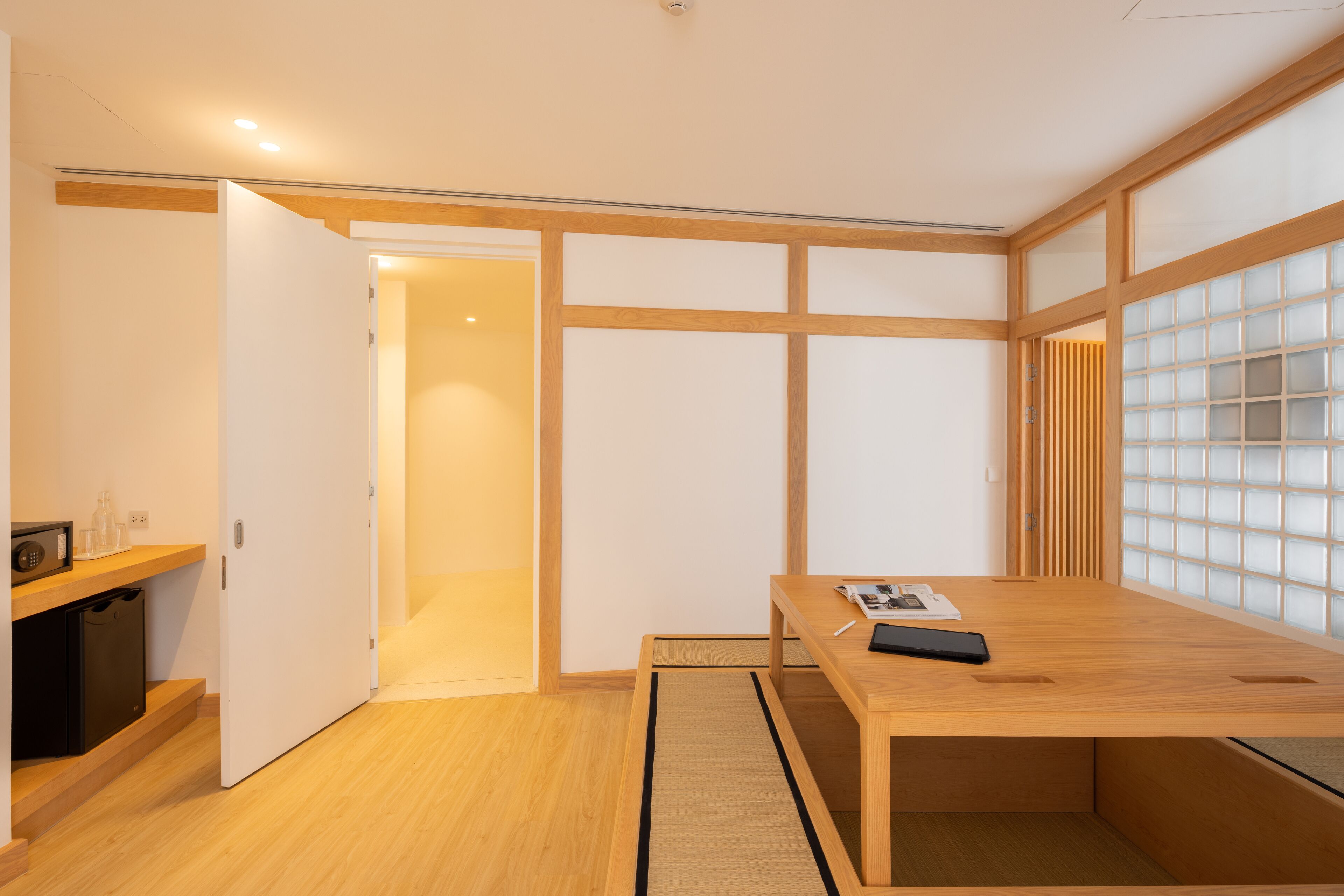 Una habitación minimalista con un escritorio de madera, un estante pequeño y una puerta corredera que da a otra habitación.