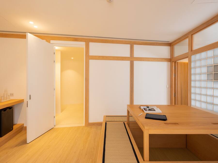 Una habitación minimalista con un escritorio de madera, un estante pequeño y una puerta corredera que da a otra habitación.