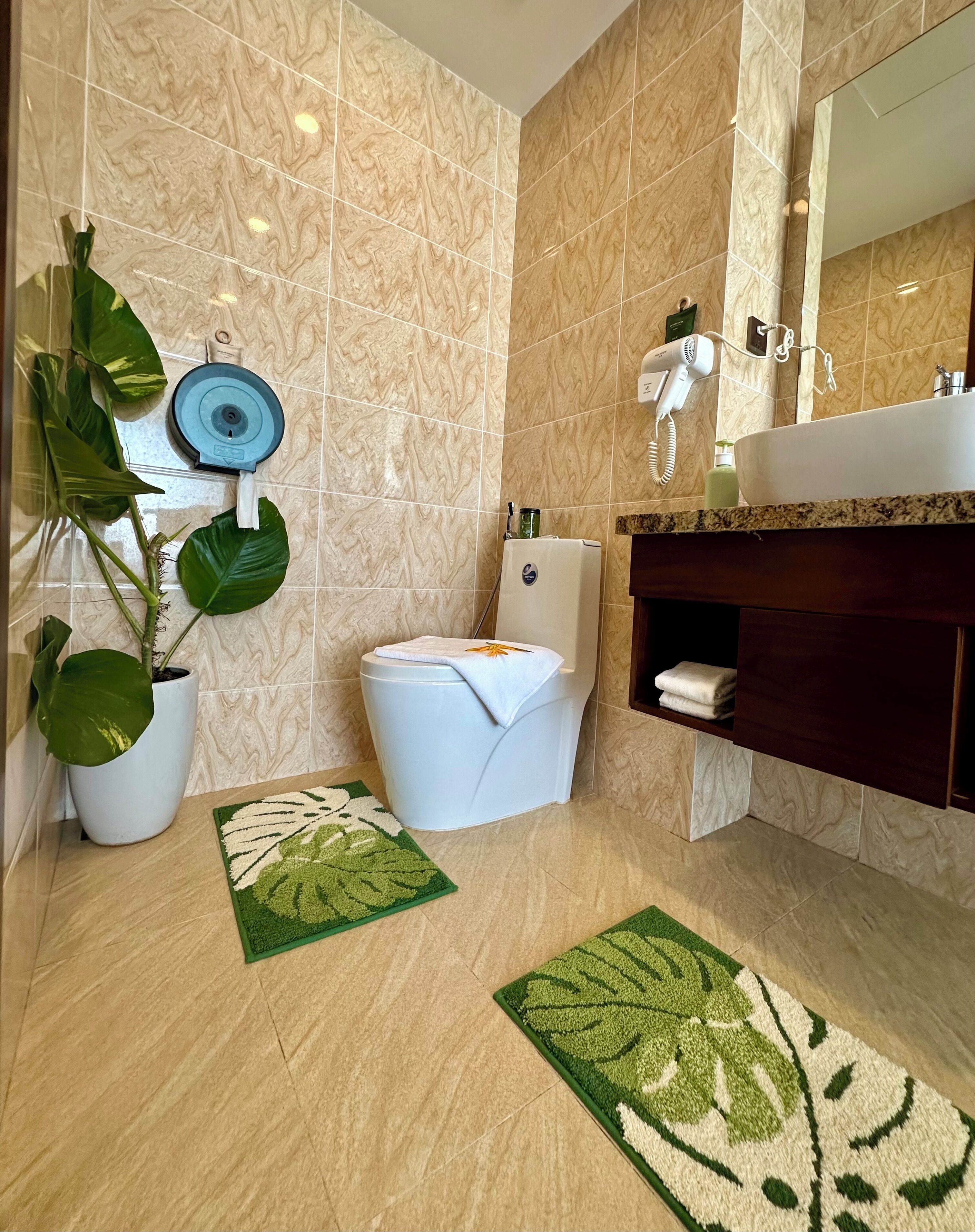 A modern bathroom with a marble backsplash, a white toilet, a sink with a mirror, and two green area rugs.