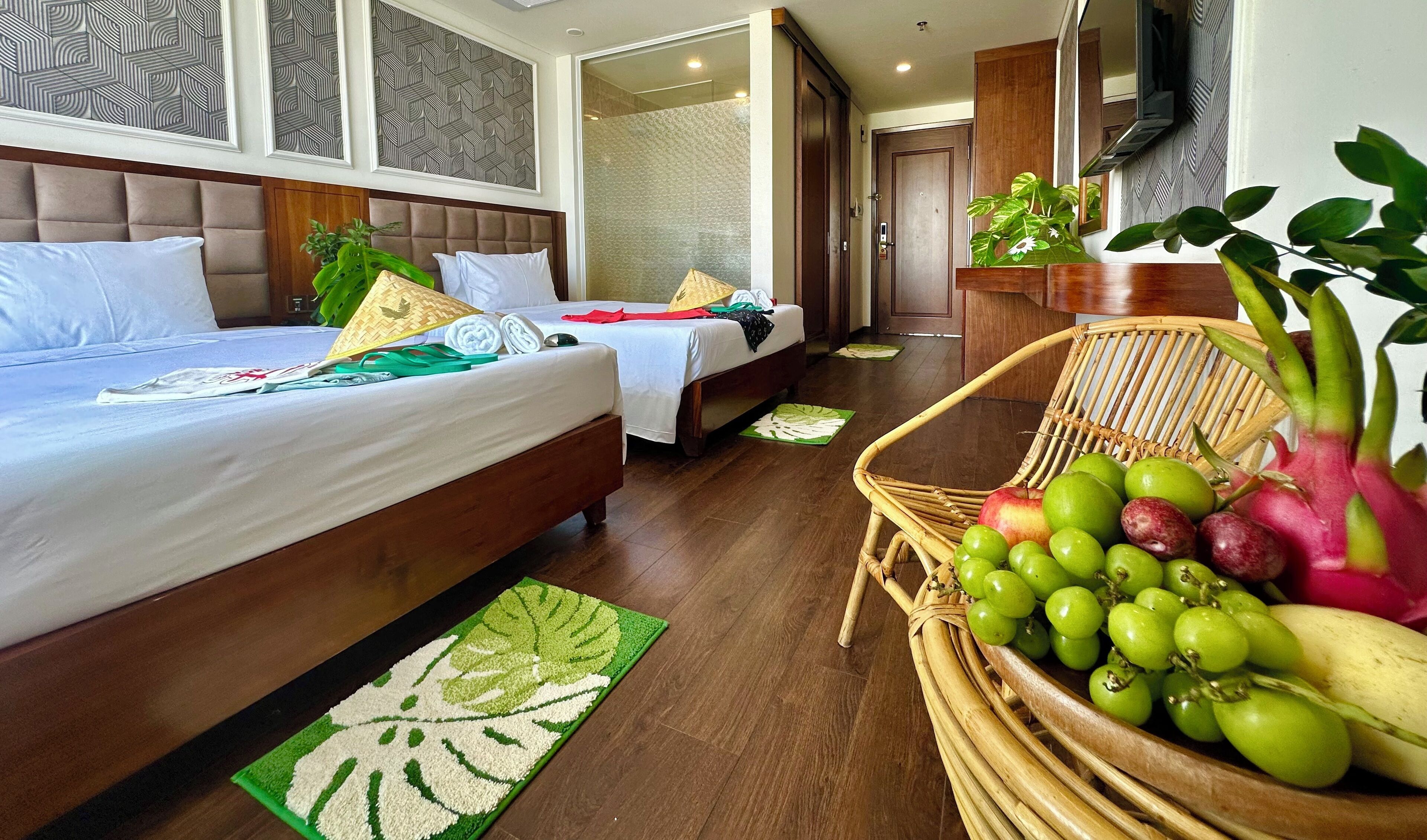 Habitación de hotel con dos camas, un ventanal grande y una cesta de mimbre con frutas.