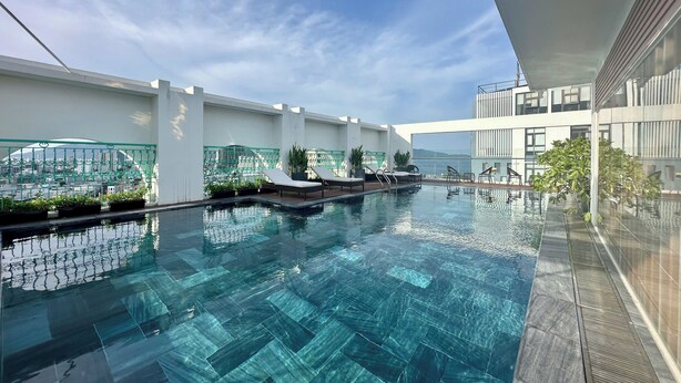 A rooftop swimming pool with clear blue water, surrounded by potted plants and lounge chairs. - Century Hotel (Da Nang)