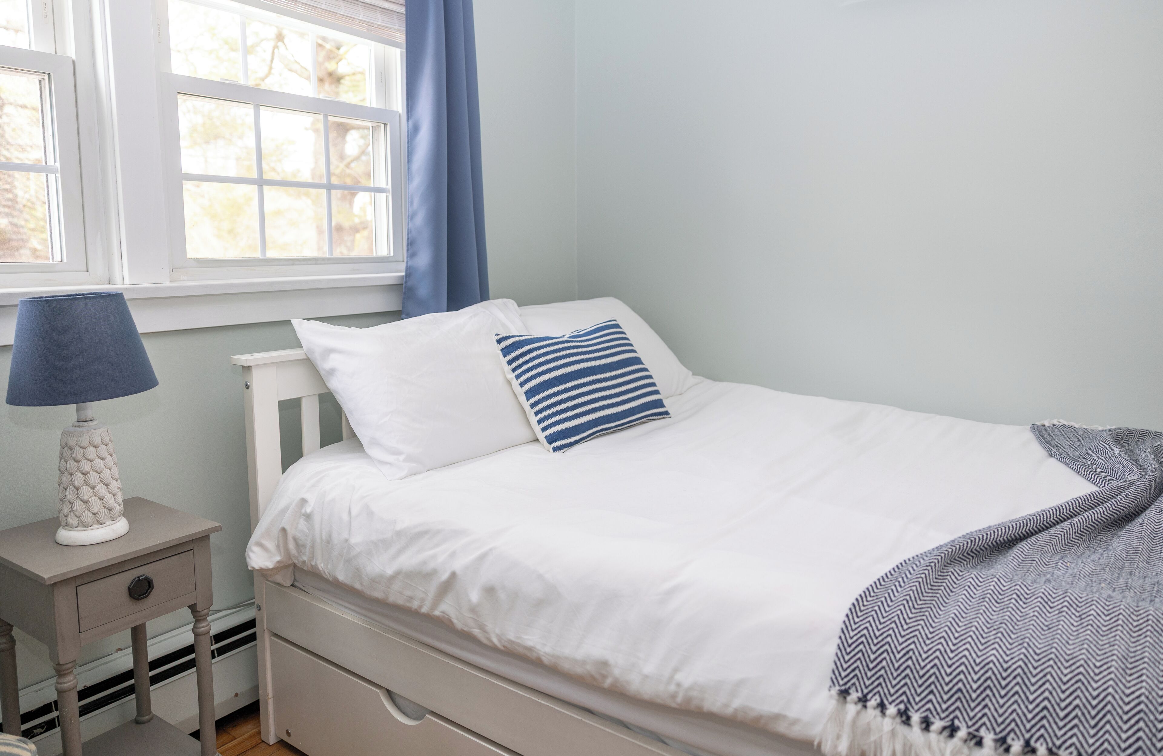 A bedroom with a bed, a nightstand, a lamp, and a window with curtains.