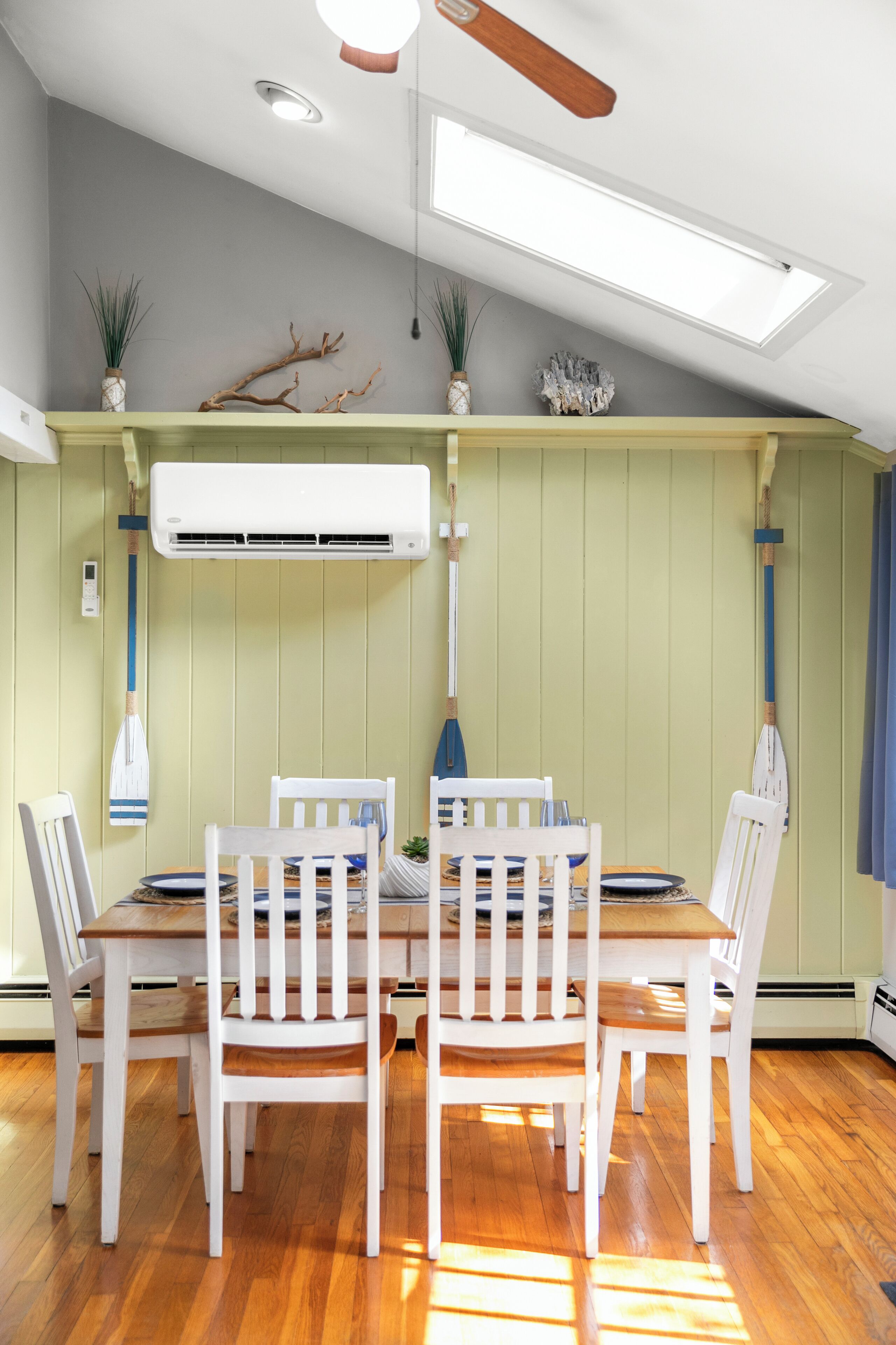 Et spiseområde med et træbord og hvide stole, en klimaanlæg og dekorative planter.