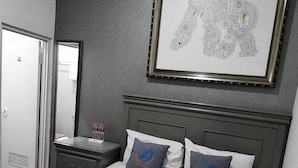 Habitació d'hotel amb un llit, una tauleta de nit, una obra d'art amb marc i una porta.