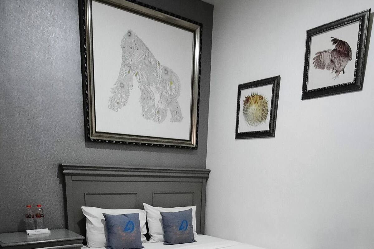 A bedroom with a bed, a nightstand, a dresser, and framed artwork on the wall.