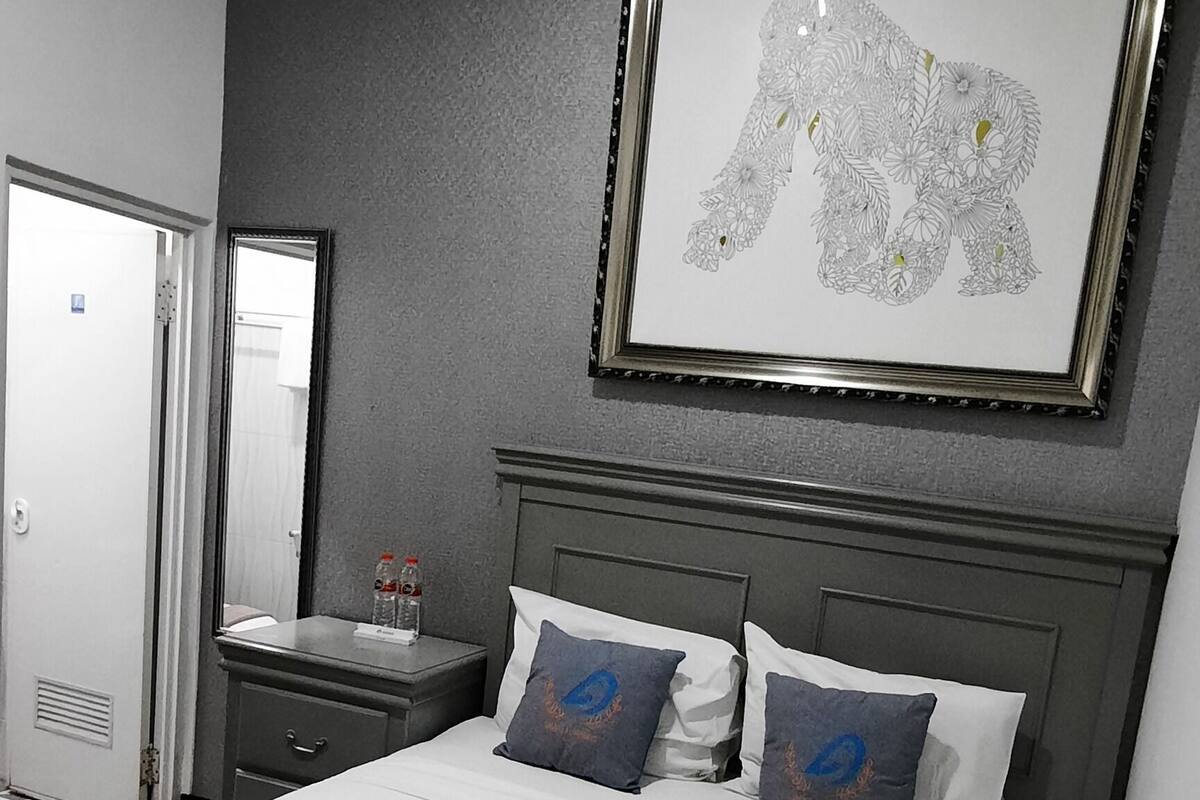 A hotel room with a bed, a nightstand, a framed artwork, and a door.