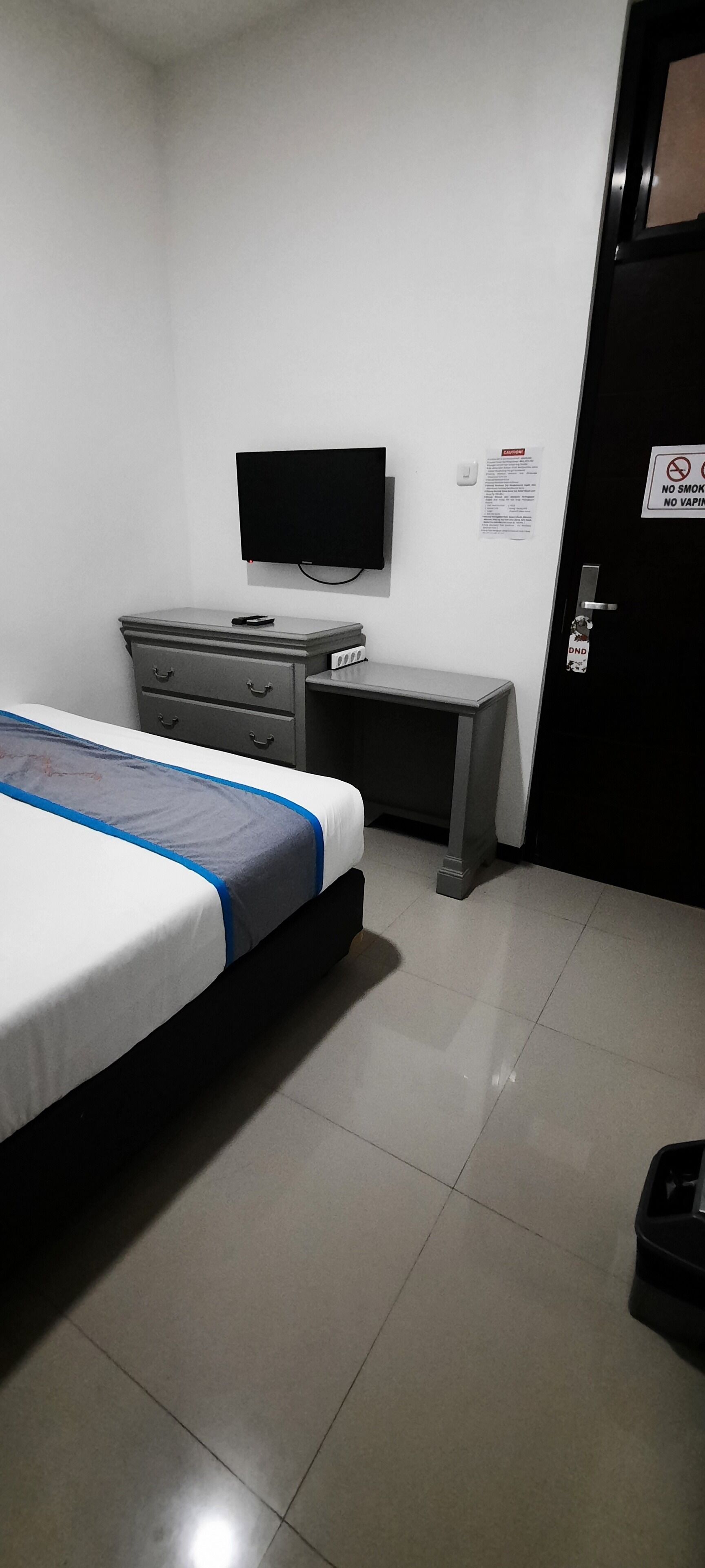 Une chambre d’hôtel équipée d’un lit, d’un bureau, d’une télévision et d’une porte sur laquelle est apposé un panneau interdisant de fumer.