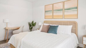 Ein Schlafzimmer mit einem großen Bett, einem Schreibtisch und einem Stuhl. Darüber befinden sich drei an der Wand befestigte Bilder.