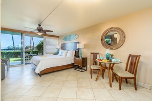 A bedroom with a bed, a ceiling fan, a dining table with chairs, a mirror, and a view of the outdoors.