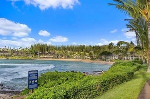 Vista costera con un letrero de advertencia, playa y edificios de un complejo turístico.
