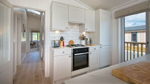 A modern kitchen with white cabinetry, a gas stove, and a large window overlooking a wooden deck. - Crabtree Lodge -  a lodge that sleeps 6 guests  in 3 bedrooms (Gatehouse Of Fleet)