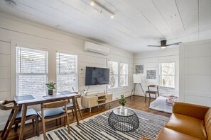 A spacious living room with a wooden dining table, chairs, a TV, and a sofa.