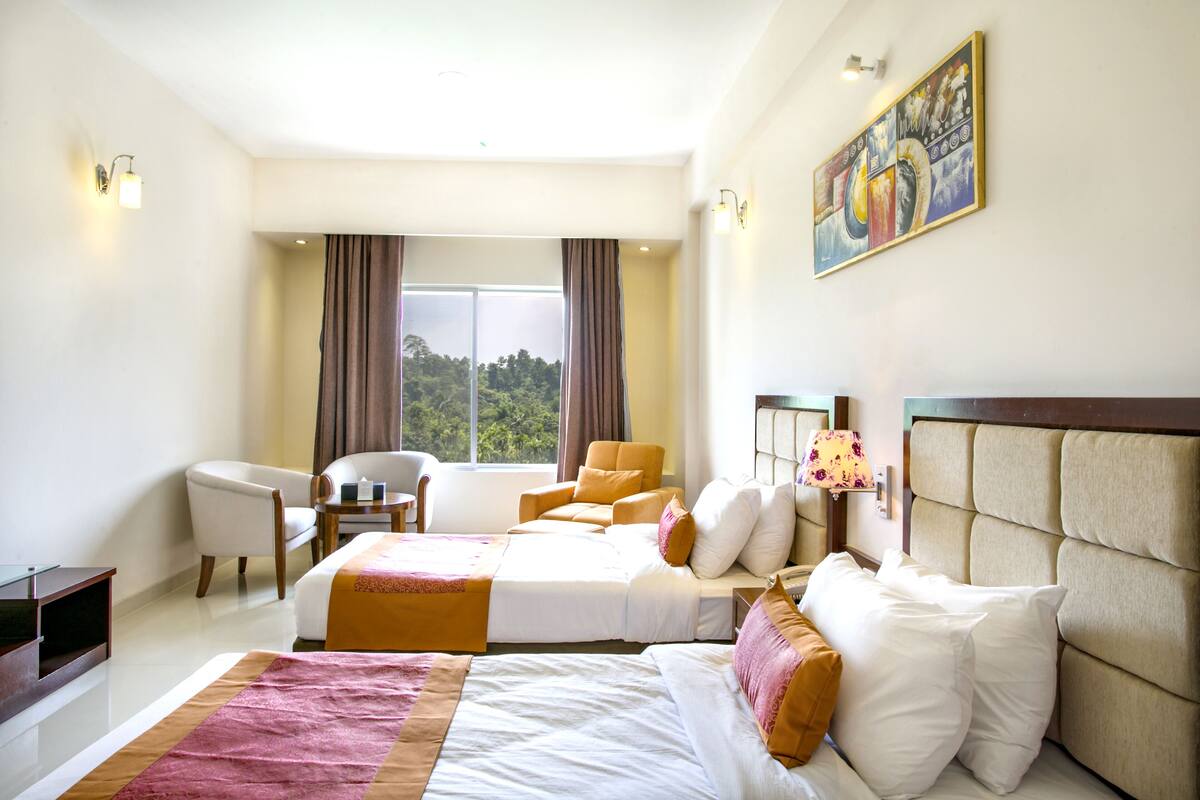 Une chambre d’hôtel avec deux lits, un coin salon avec une chaise et une table, et une grande fenêtre avec des rideaux.