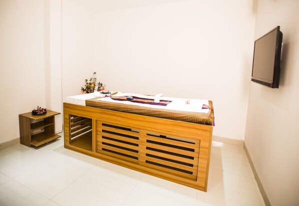 Un comptoir d’accueil avec un plateau blanc et une base en bois, une petite table d’appoint avec un panier, et un téléviseur à écran plat fixé au mur.
