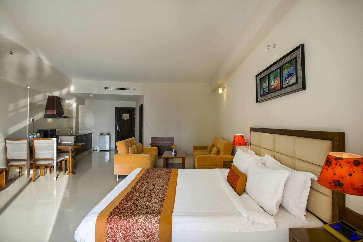 Une chambre d’hôtel avec un grand lit, deux fauteuils, une petite table, un bureau et une kitchenette.