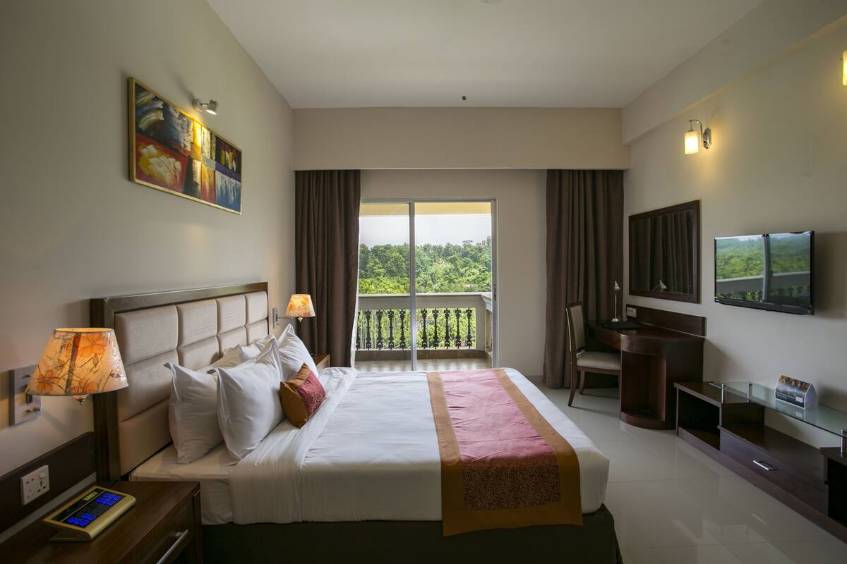 Une chambre d’hôtel avec un grand lit, une télévision, un bureau et un balcon donnant sur la verdure.