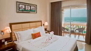 A hotel room with a large bed, a nightstand with a lamp, a framed picture above the bed, and a balcony with a view of the ocean. - Sea Pearl Beach Resort & Spa Cox's Bazar (Cox's Bazar)