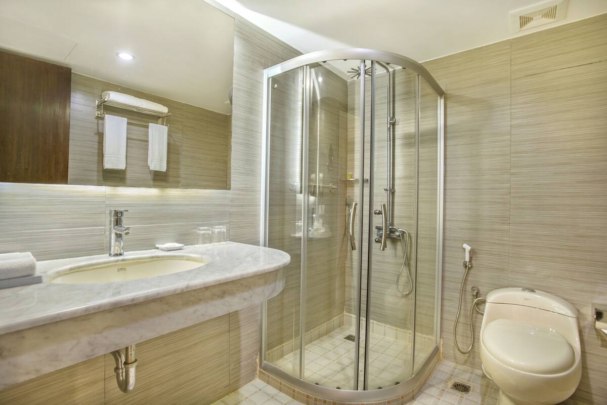 Une salle de bain moderne avec une douche à l’italienne dotée de parois en verre incurvé, un lavabo en marbre et des toilettes.