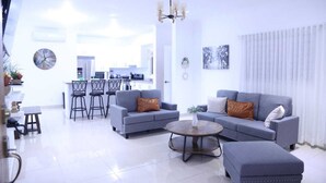 Un salon moderne avec un canapé gris, une table basse et un coin repas agrémenté d’un lustre.