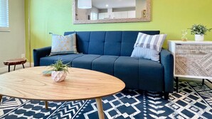 Una sala de estar con un sofá azul, una mesa de centro redonda de madera y un tapete estampado.