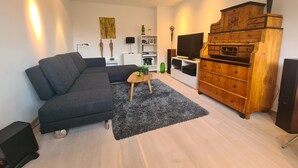 Un salon moderne avec un canapé d’angle, un meuble en bois, un téléviseur à écran plat et une petite table agrémentée d’objets décoratifs.